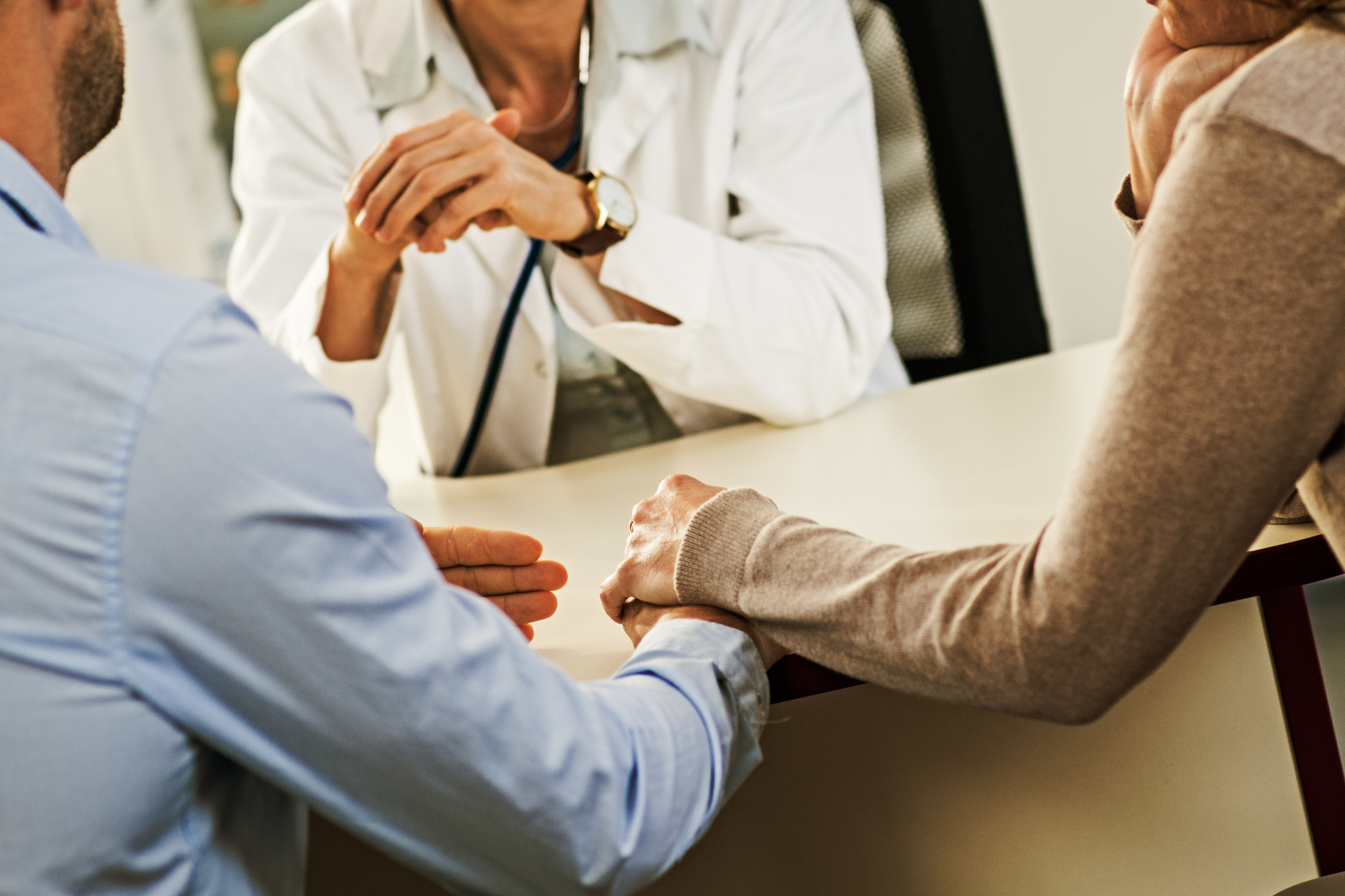 Worried mature couple holding hands while listening to female doctor.